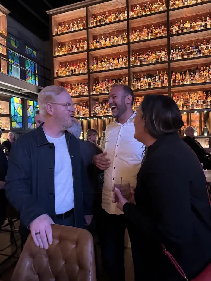 Three people talking in front of a wall of whiskey bottles