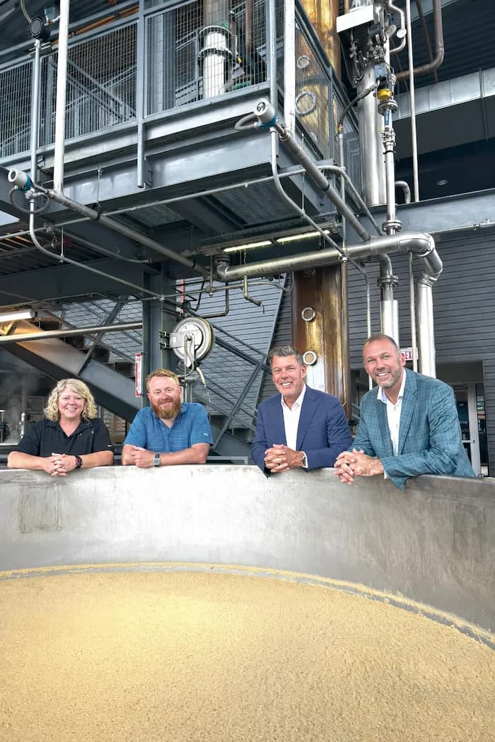 Four people leaning over a mash tun at a distillery
